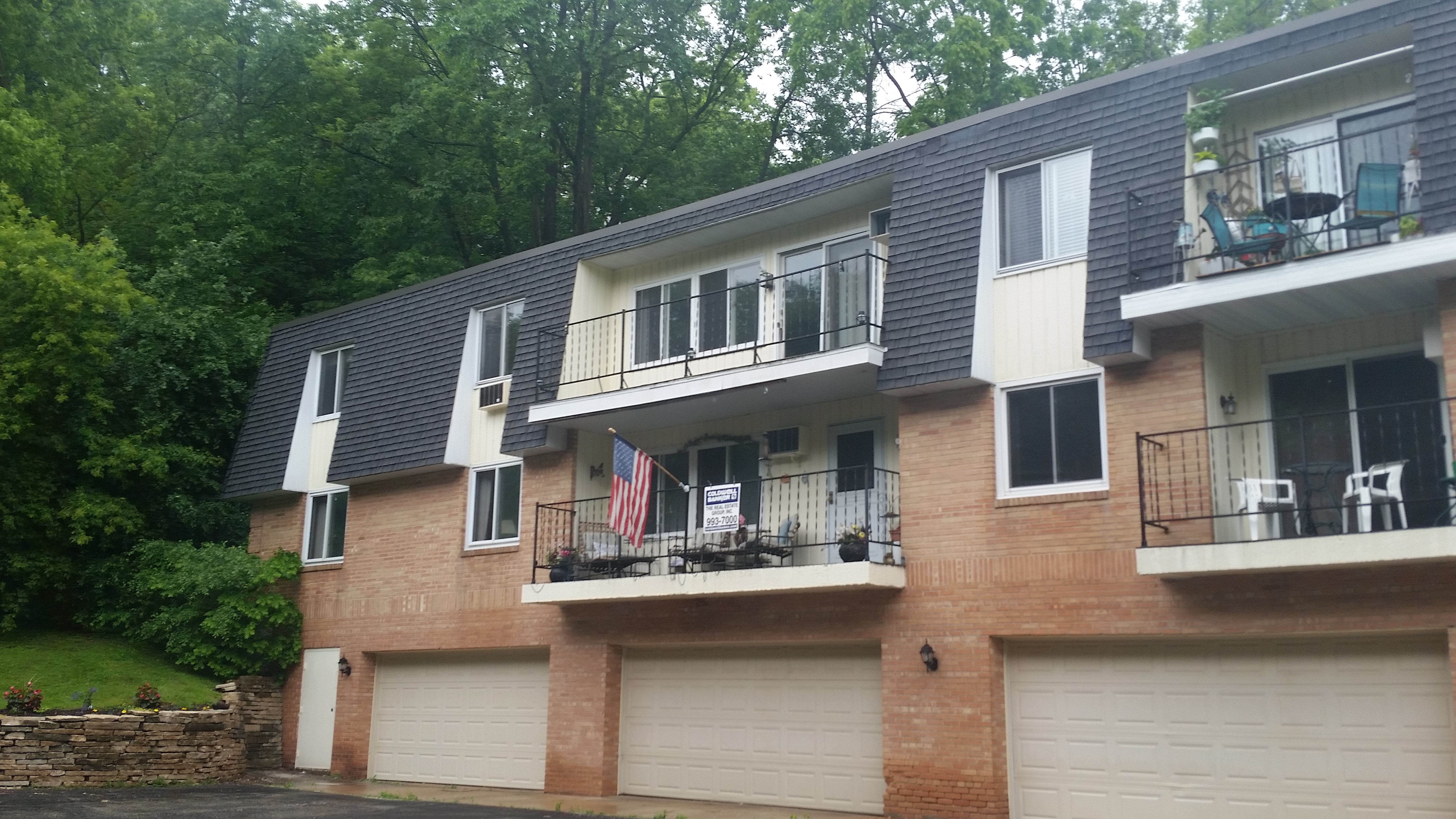 Exterior shot of apartment building in a suburban location with garage doors, balconies, and greenery in the background.