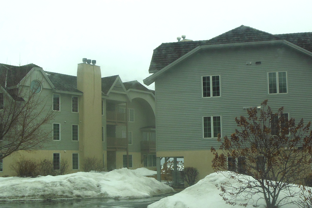 Exterior of gray, three story condo building during an overcast winter day. There are snowbanks seen on the ground.