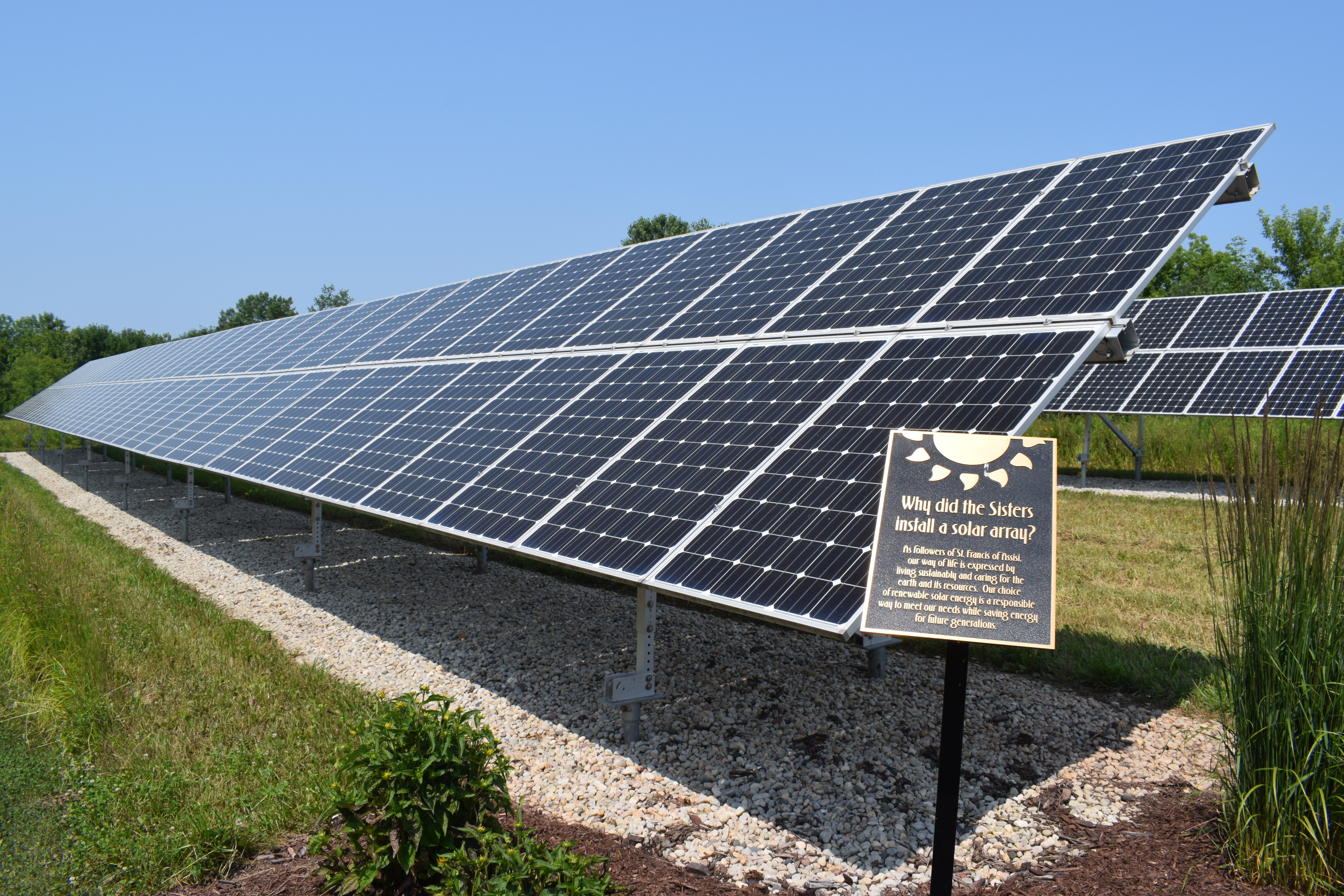 Solar array in an outdoor space with a plaque that reads "Why did the Sisters install a solar array?"