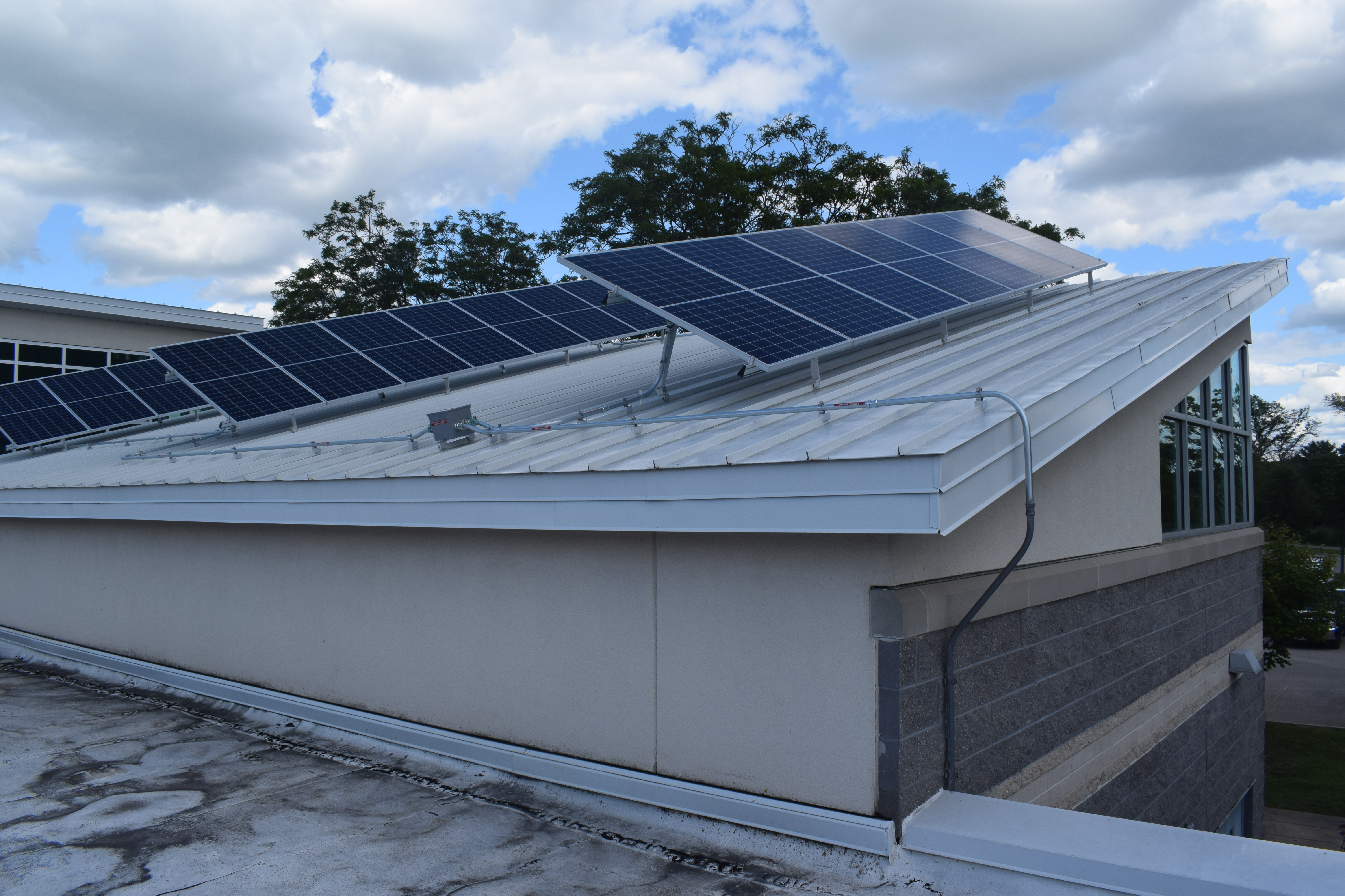 Three rows of solar panels are installed on a slanted, metal rooftop of a modern building. 