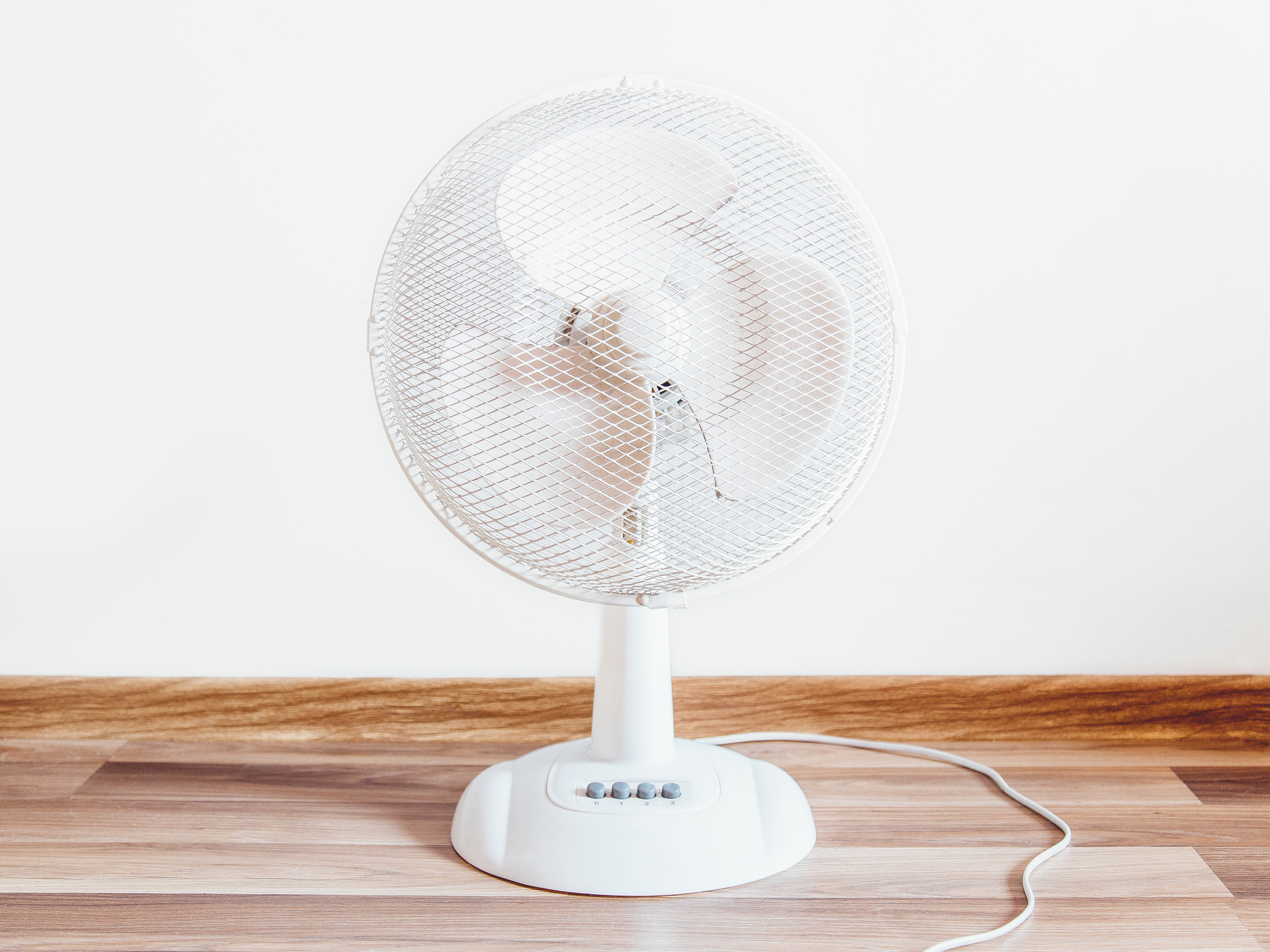 A white fan sits on a wooden floor in front of a white background.