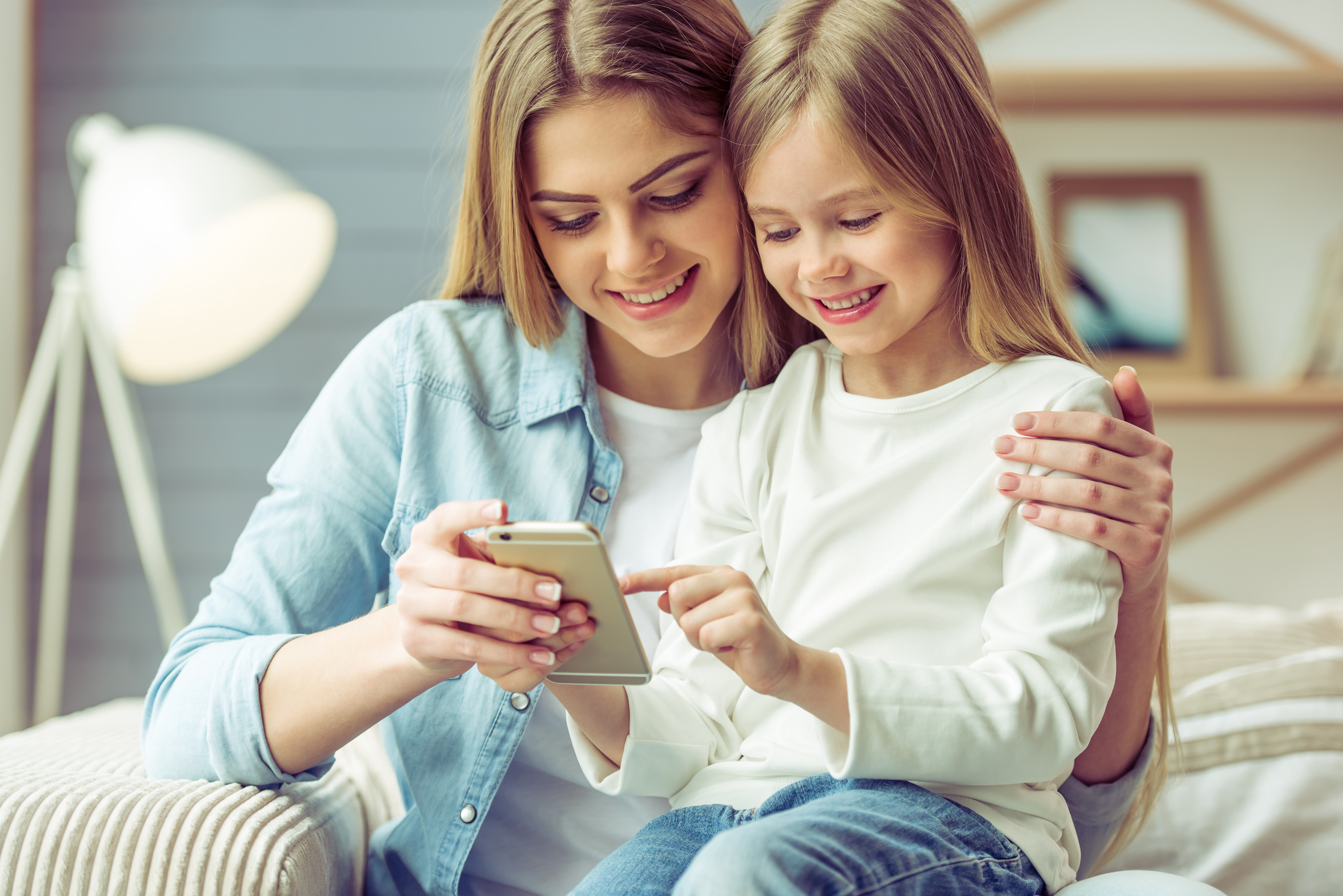 A young woman and a child sit together on a couch, looking at a smartphone together.