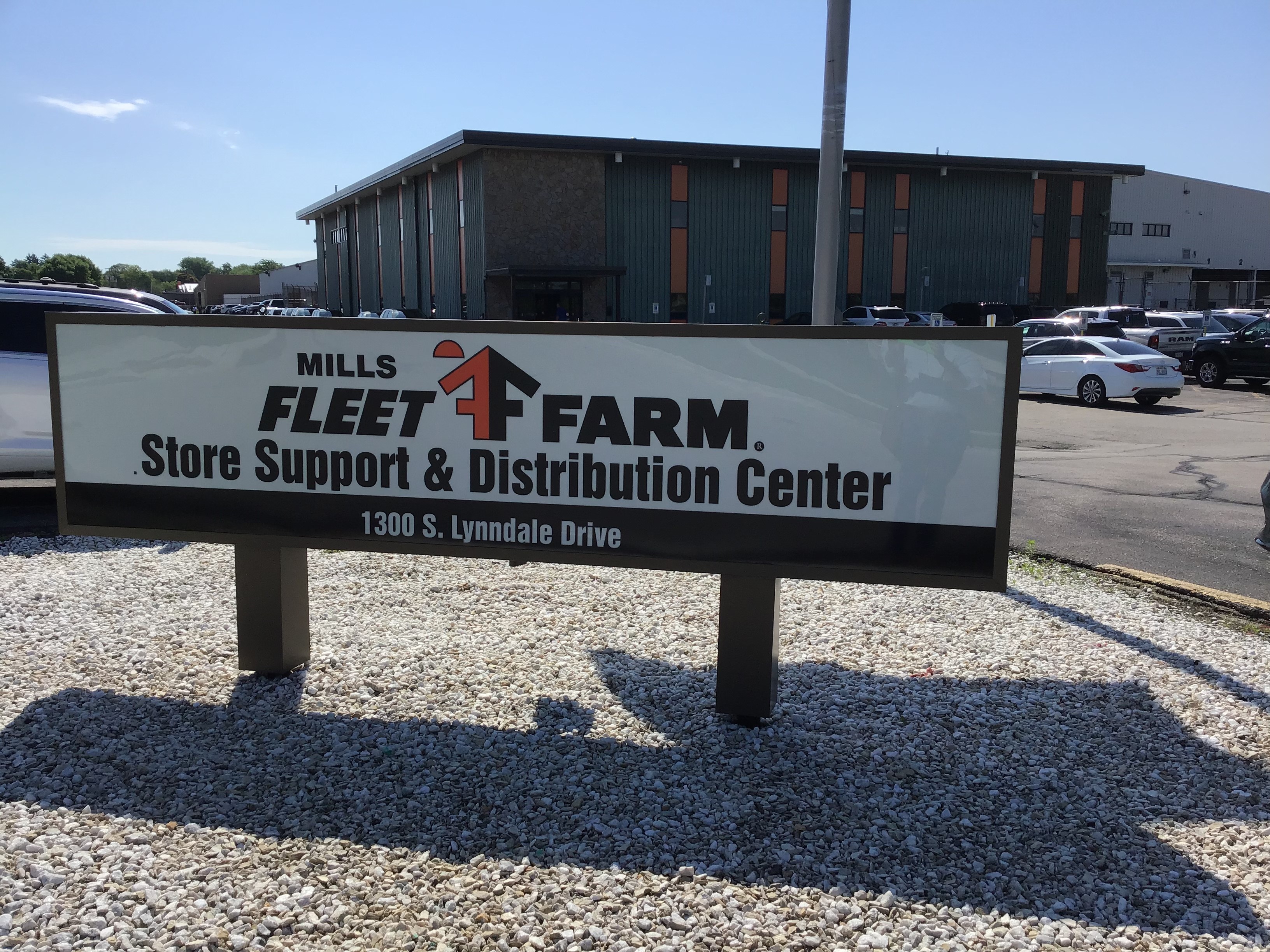 Fleet farm sign in a parking lot that reads "Mills Fleet Farm Store Support & Distribution Center" with the address 1300 S. Lynndale Drive at the bottom of the sign.