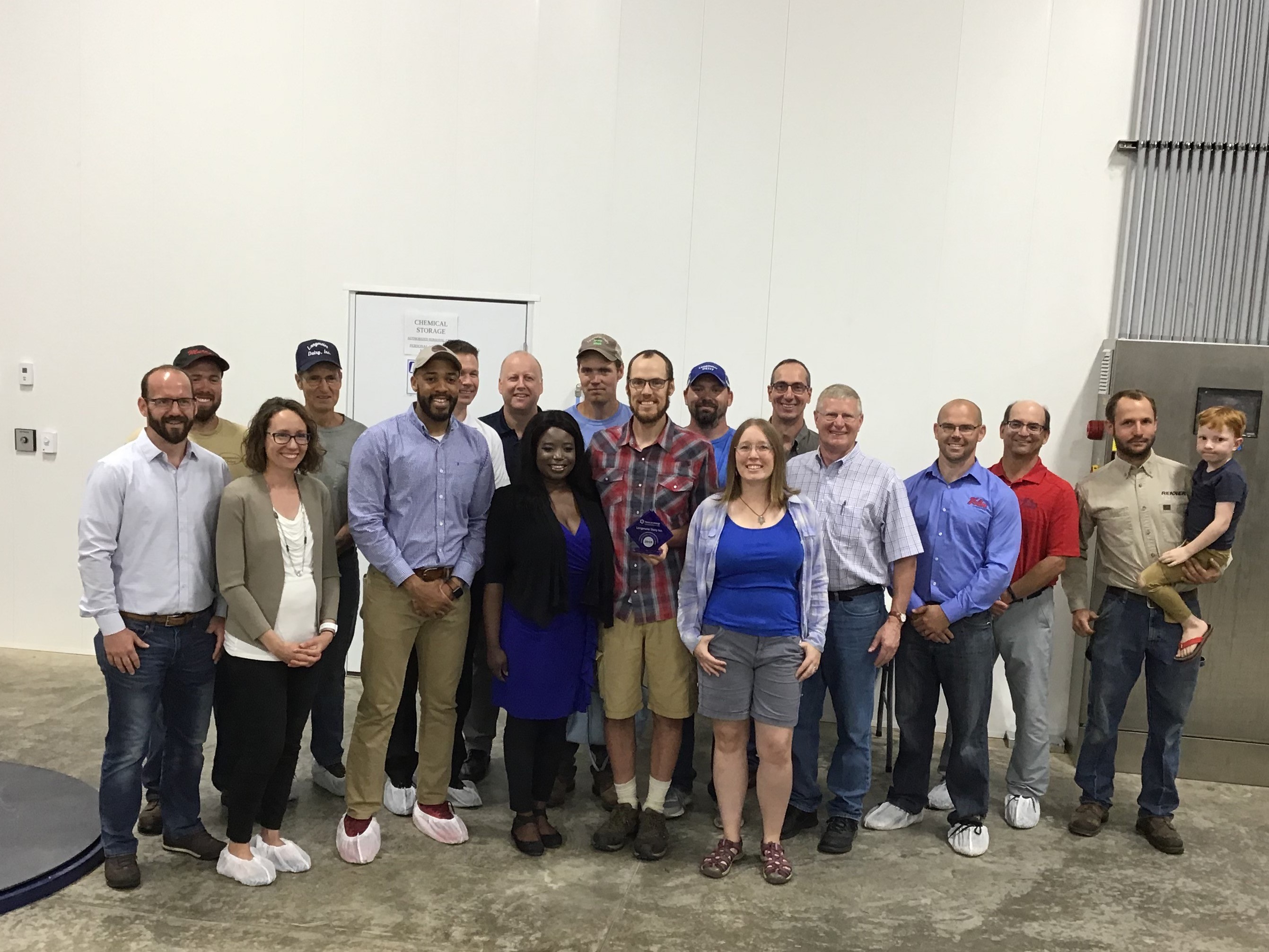 Group photo of several people in a warehouse. A man in the middle is holding the blue, diamond shaped award from Focus on Energy.