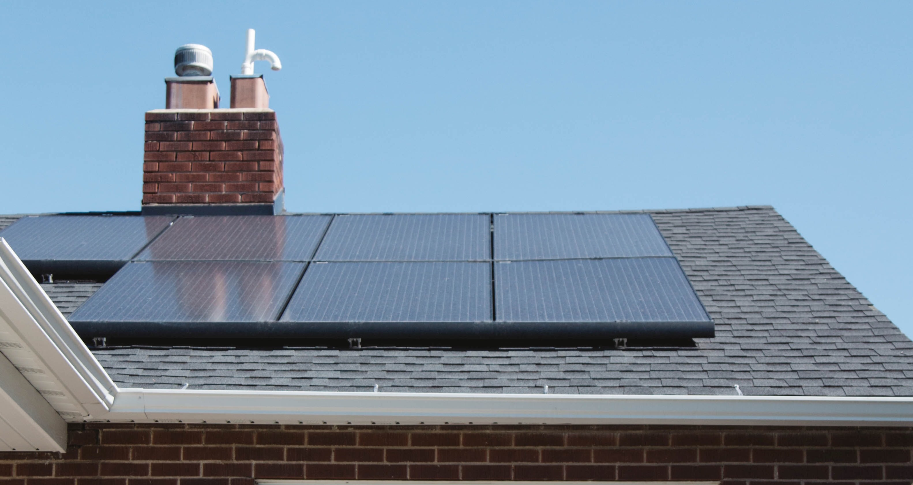 Solar panels on a rooftop with a chimney in the background. 